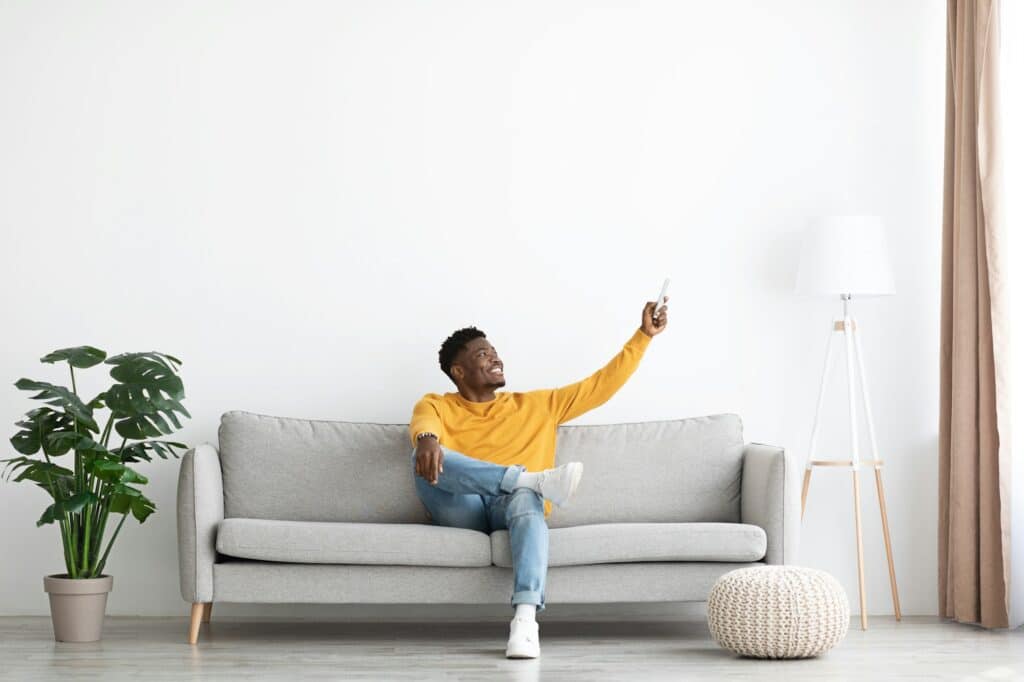 Essential Tips for HVAC System Care as Summer Approaches Relaxed african american guy sitting on couch, turning on AC
