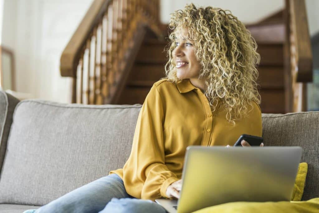 Cheerful adult lady with blonde long curly hair work at home on laptop computer comfortably