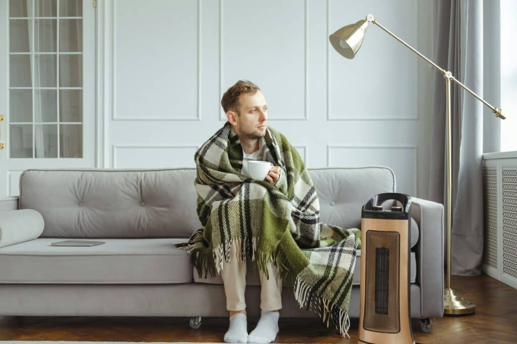 Young man in wrapped in plaid in warm clothes with cup of tea at home. Concept of heating season