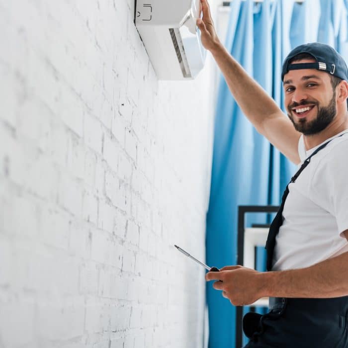 Smiling workman looking at camera while repairing air conditioner